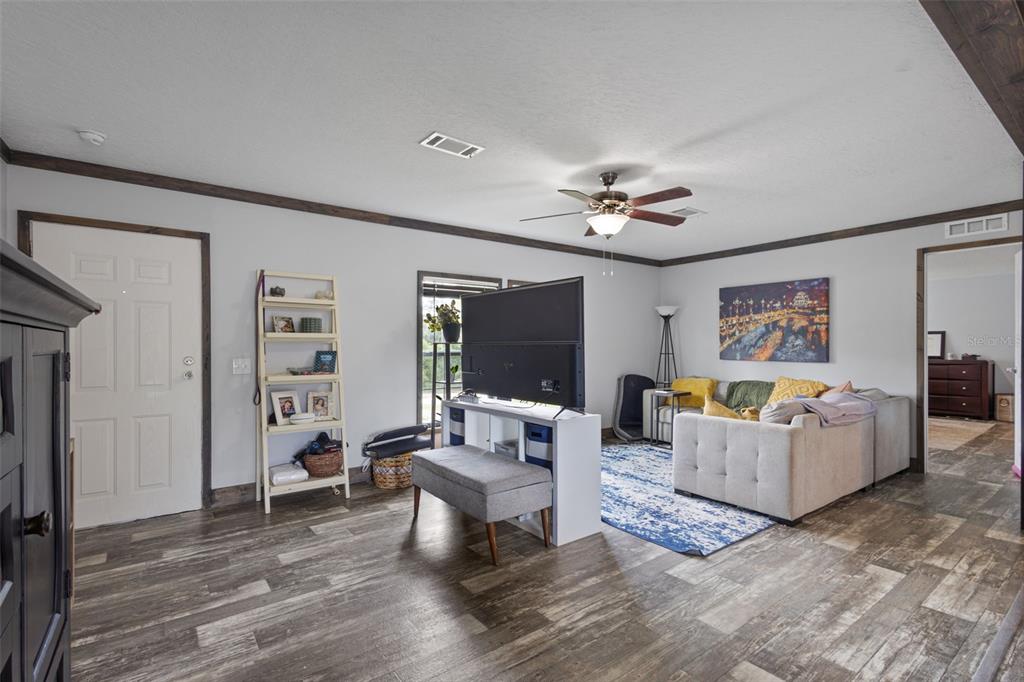 A living room features wood-look flooring, a ceiling fan, a sectional sofa, and a television stand — 9490 NE 77TH PLACE, BRONSON, FL
