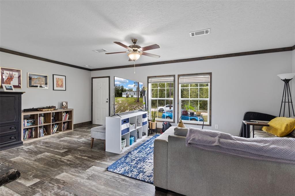 A living room features wood-look flooring, a ceiling fan, a bookshelf, and a television stand — 9490 NE 77TH PLACE, BRONSON, FL