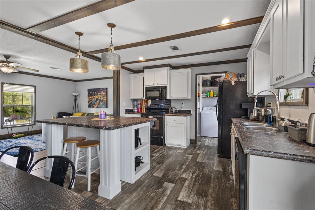 A kitchen with white cabinets, a dark island, wood-look flooring, and exposed ceiling beams — 9490 NE 77TH PLACE, BRONSON, FL