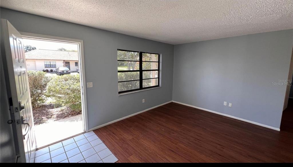 An empty room with light blue walls, wood-look flooring, a window, and an open door — 9103 WHITMAN LANE, PORT RICHEY, FL