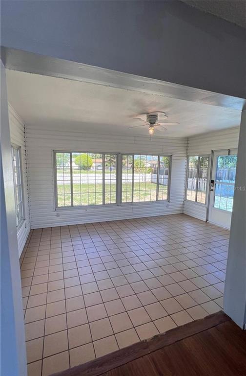 A sunroom with white horizontal wall paneling, tiled flooring, and large windows overlooking a yard — 9103 WHITMAN LANE, PORT RICHEY, FL