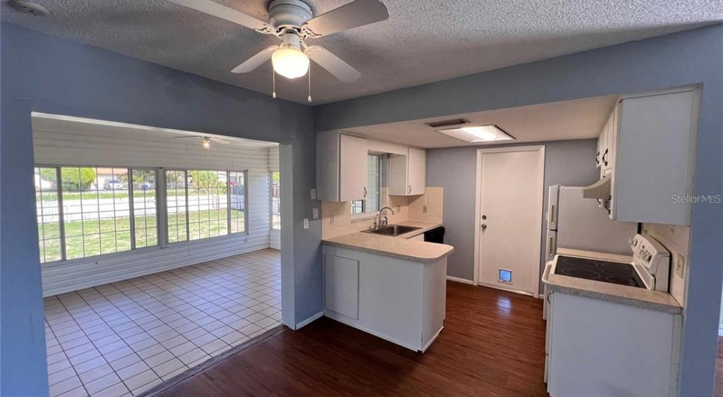 A kitchen with white cabinets and wood-look flooring opens to a tiled sunroom with windows — 9103 WHITMAN LANE, PORT RICHEY, FL
