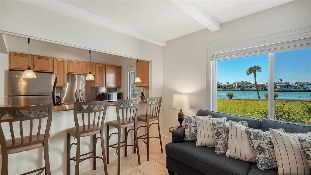 A kitchen with wooden cabinets and a breakfast bar overlooks a living area with water views — 761 JOHN RINGLING BOULEVARD UNIT 5, SARASOTA, FL