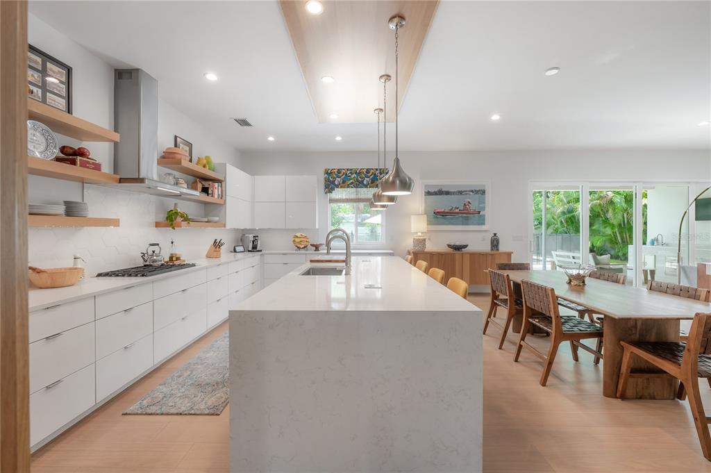 A modern kitchen features white cabinetry, a large quartz island, and a wooden dining table — 4207 W JETTON AVENUE, TAMPA, FL