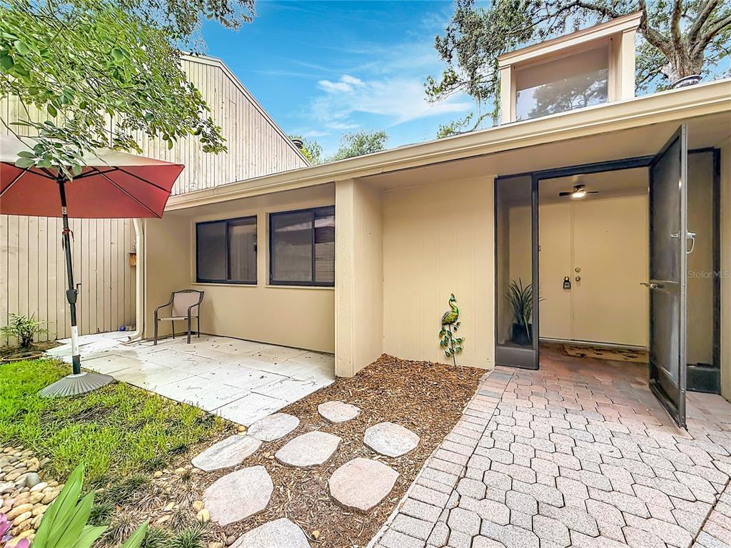 A paved walkway leads to the front entrance of a house with a patio area — 111 JUNIPER LANE, LONGWOOD, FL