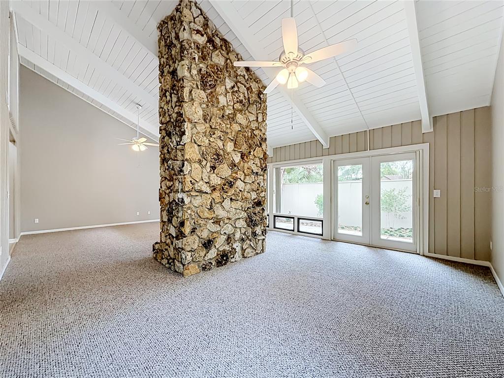 A living room features a central stone fireplace, vaulted ceilings, and glass patio doors — 111 JUNIPER LANE, LONGWOOD, FL