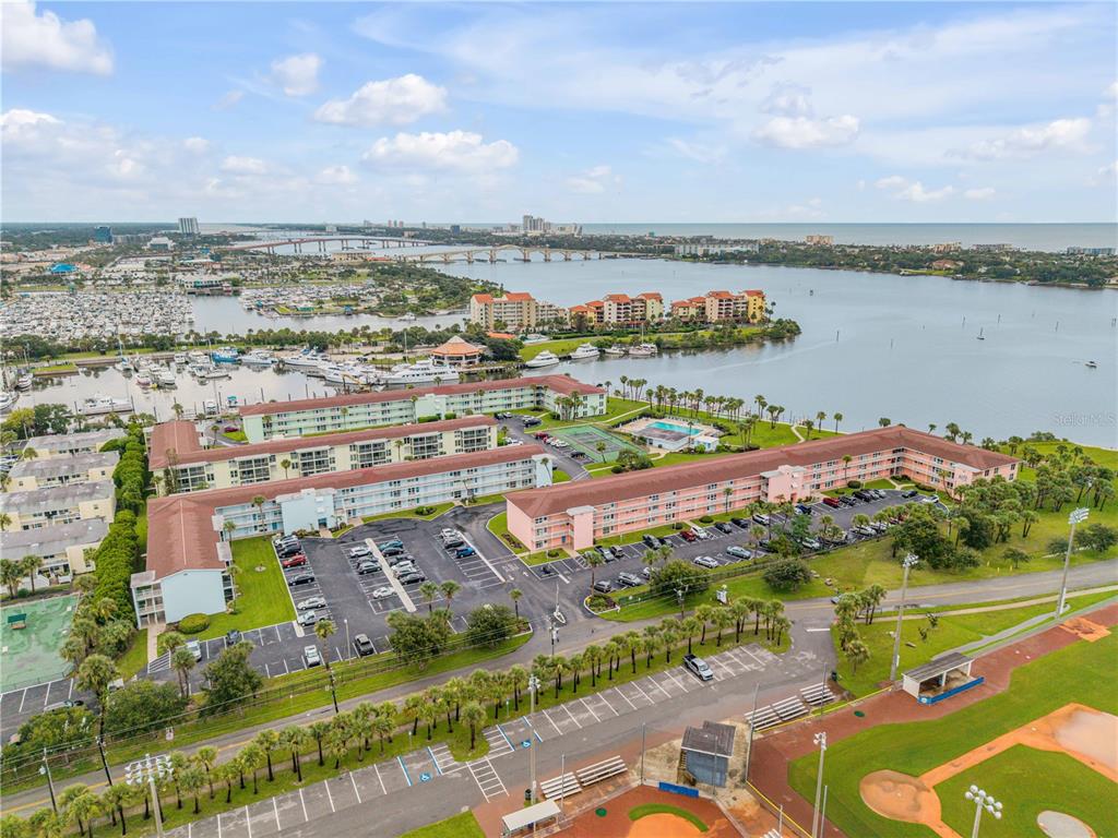 An aerial view shows a multi-story apartment complex with parking lots, tennis courts, and waterfront — 715 S BEACH STREET UNIT 214D, DAYTONA BEACH, FL