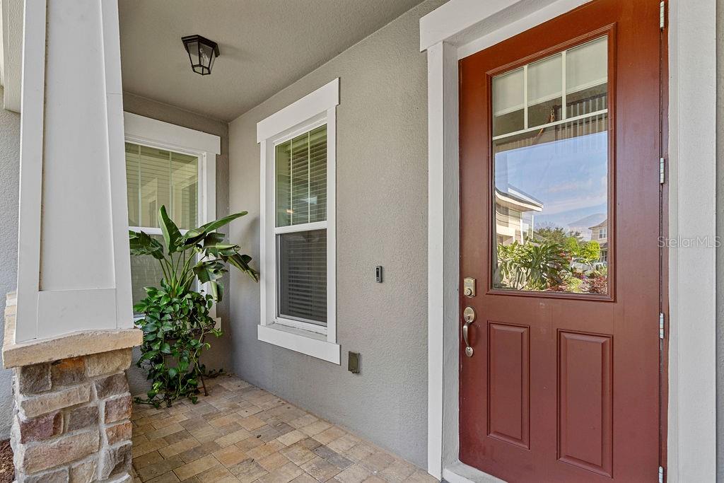 A covered front porch features a red door, stone base pillar, and a potted plant — 14897 ELLINGSWORTH LANE, WINTER GARDEN, FL