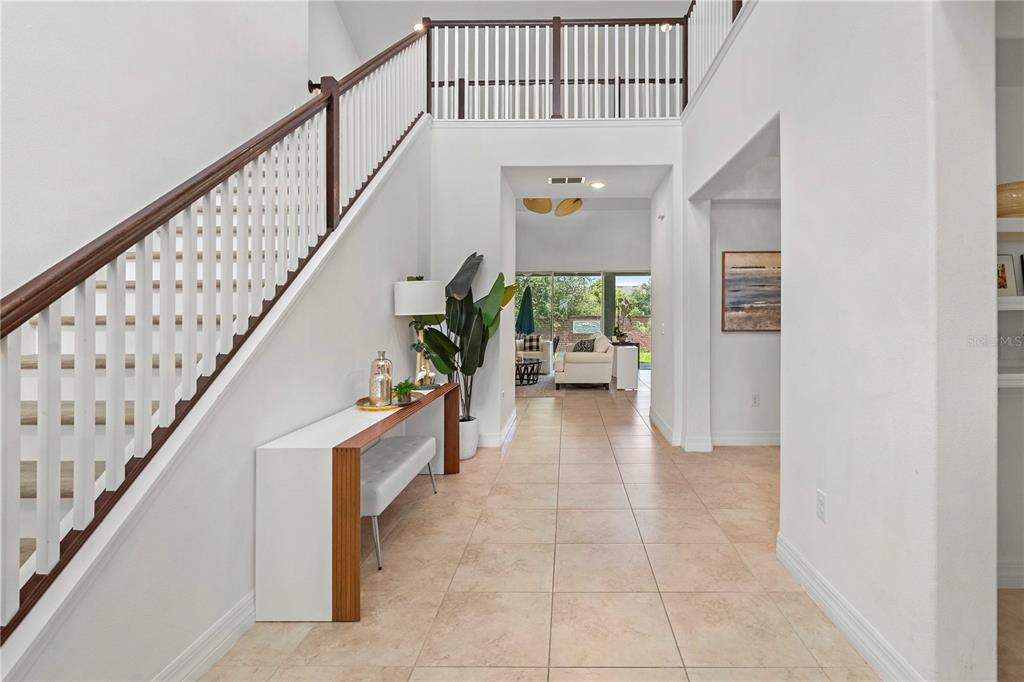 A bright foyer features a staircase with a wooden railing and tile flooring — 14897 ELLINGSWORTH LANE, WINTER GARDEN, FL