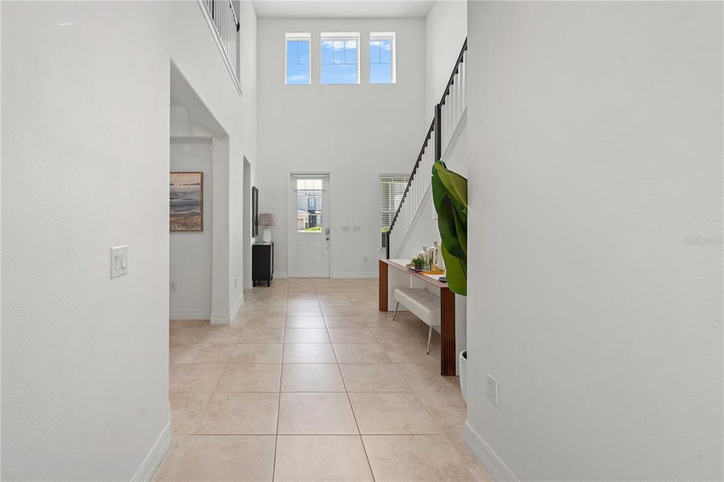A bright entryway features high ceilings, tile flooring, a staircase, and a front door — 14897 ELLINGSWORTH LANE, WINTER GARDEN, FL