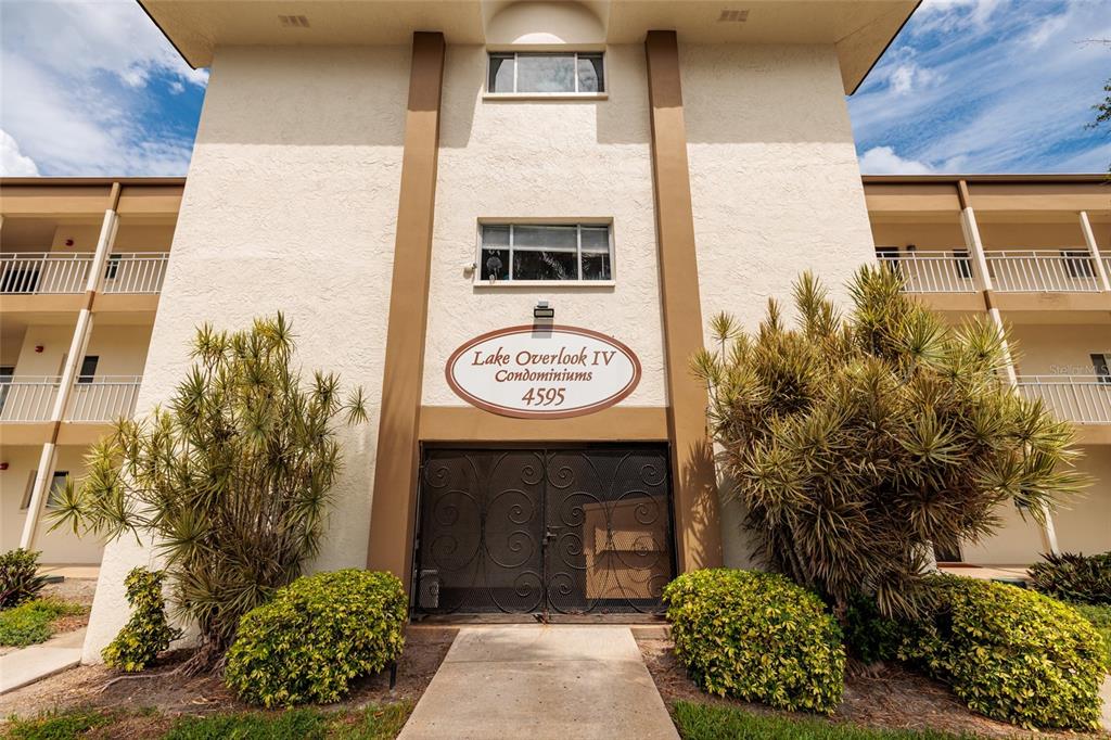 The exterior of a multi-story condominium building features a central entrance with a decorative gate — 4595 CHANCELLOR STREET NE UNIT 114, ST PETERSBURG, FL