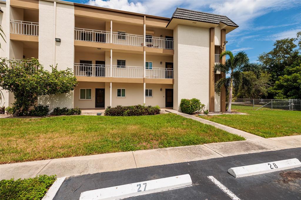 A three-story apartment building exterior with balconies and numbered parking spaces in the foreground — 4595 CHANCELLOR STREET NE UNIT 114, ST PETERSBURG, FL