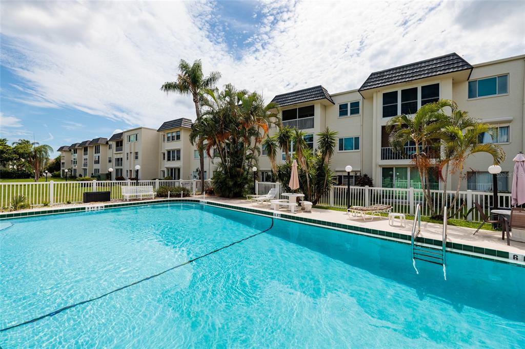A swimming pool sits in front of a multi-story apartment building with palm trees — 4595 CHANCELLOR STREET NE UNIT 114, ST PETERSBURG, FL