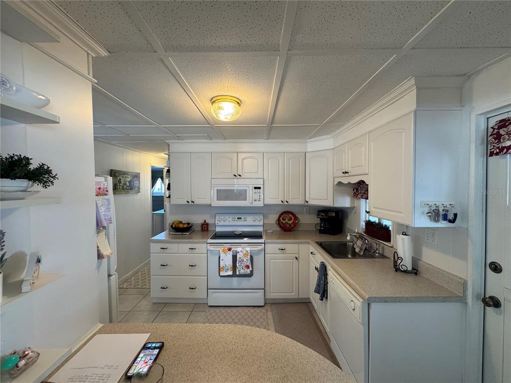 A kitchen features white cabinets, a white stove, a microwave, and a tiled ceiling — 611 IRIS DRIVE, VENICE, FL