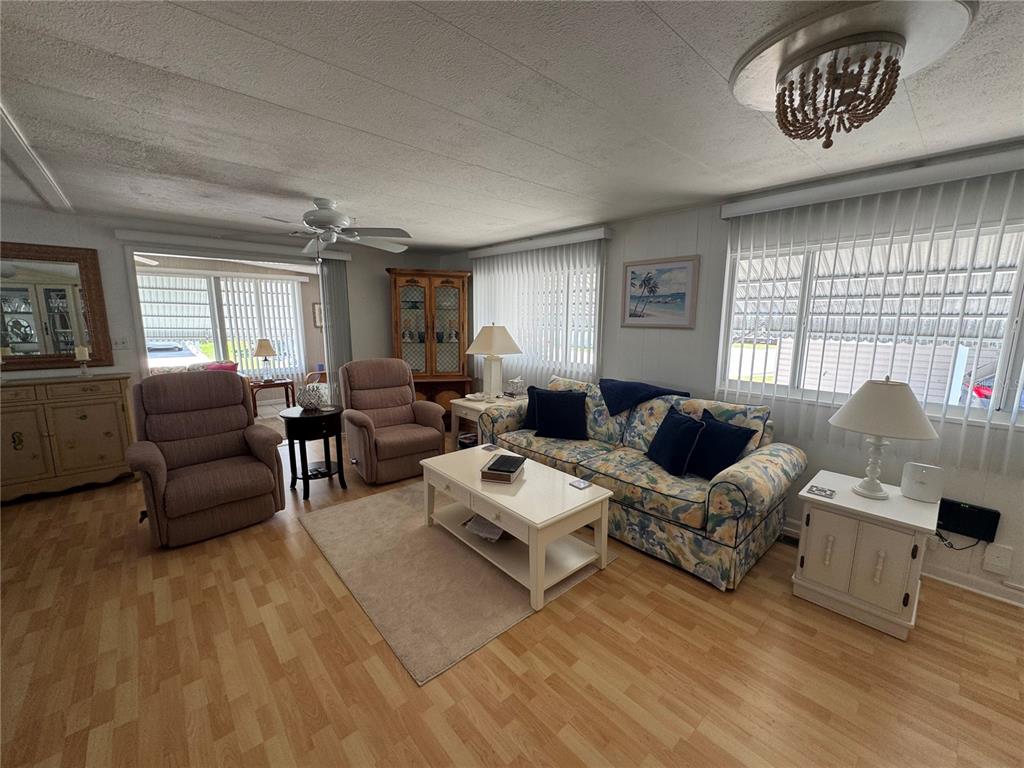 A living room features light wood-look flooring, a floral sofa, two recliners, and vertical blinds — 611 IRIS DRIVE, VENICE, FL