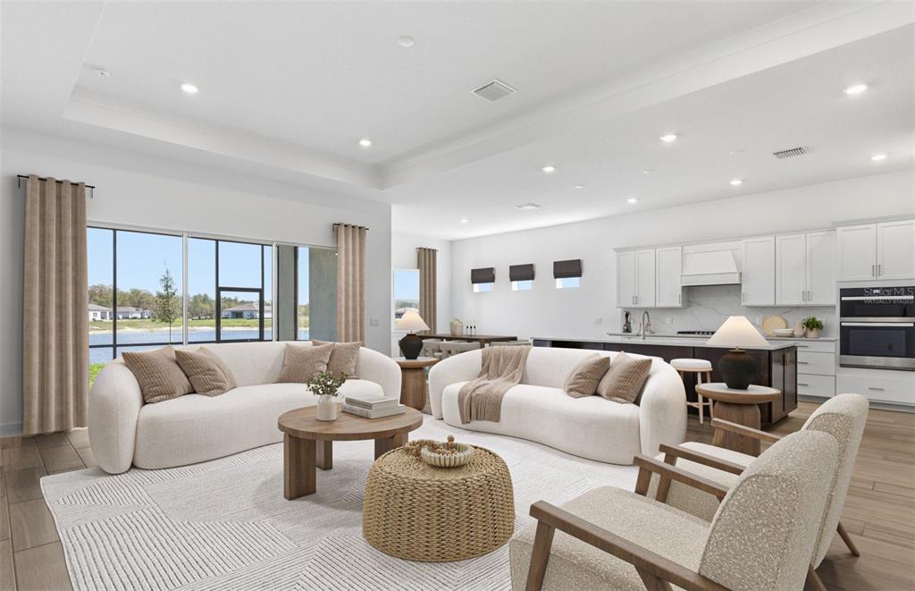 A living room with two curved sofas, a kitchen, and a view of a lake — 16694 HARVEST LEAF ROAD, SPRING HILL, FL