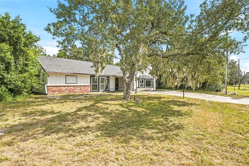 A single-story house with a brick and white exterior sits behind a large oak tree — 2112 MEADOW LARK ROAD, SPRING HILL, FL