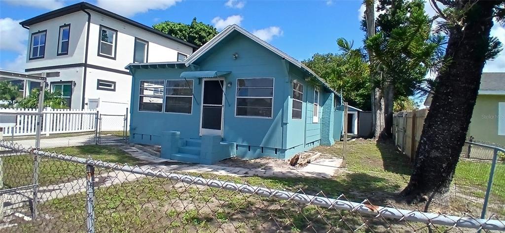 A blue single-story house stands next to a taller white building behind a chain-link fence — 2055 28TH AVENUE N, ST PETERSBURG, FL