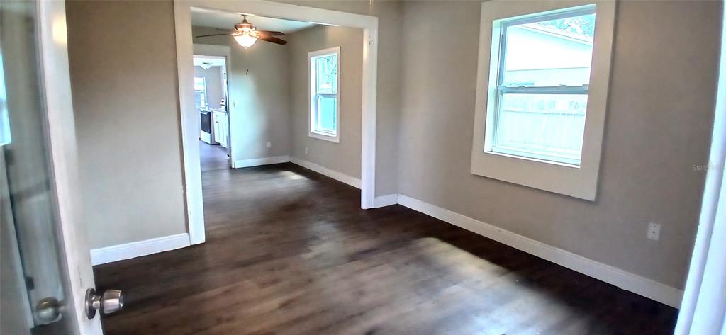 An interior view shows a room with dark wood-look flooring and a doorway to a kitchen — 2055 28TH AVENUE N, ST PETERSBURG, FL