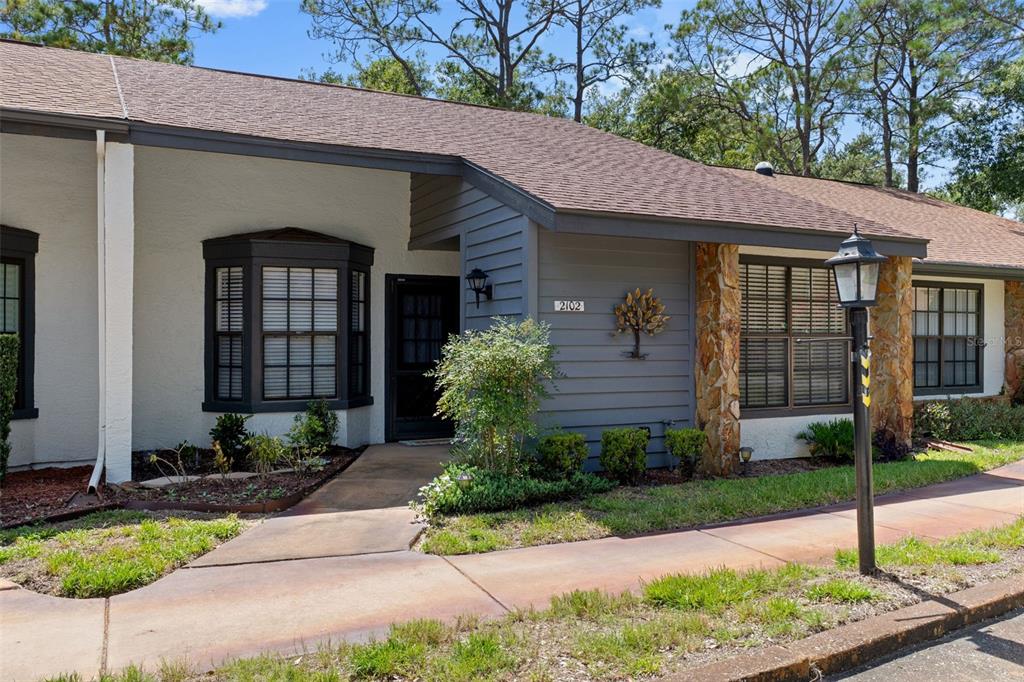 A single-story home exterior features gray siding, a stone pillar, and a bay window — 2102 FORESTER WAY, SPRING HILL, FL