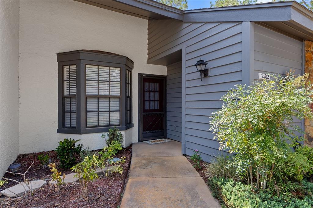 The exterior of a home features a bay window, a front door, and gray siding — 2102 FORESTER WAY, SPRING HILL, FL