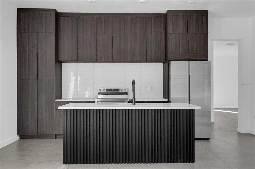 A modern kitchen features dark wood cabinetry, white countertops, a slatted island, and stainless appliances — 501 CHASTAIN ROAD, SEFFNER, FL