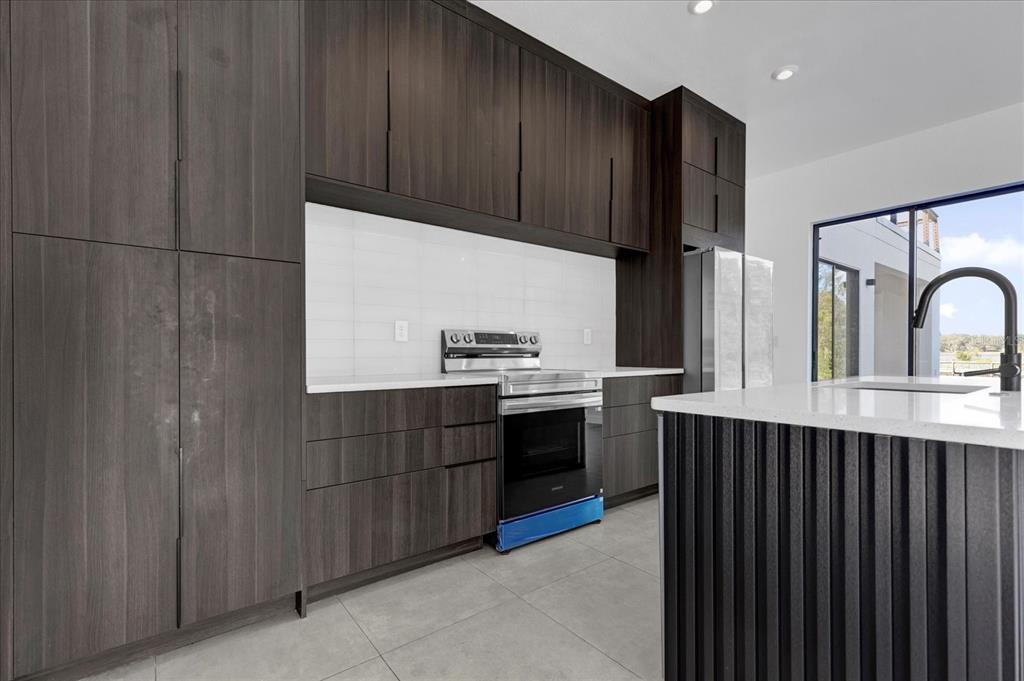 A modern kitchen features dark wood cabinetry, white countertops, a stainless steel range, and tile flooring — 501 CHASTAIN ROAD, SEFFNER, FL