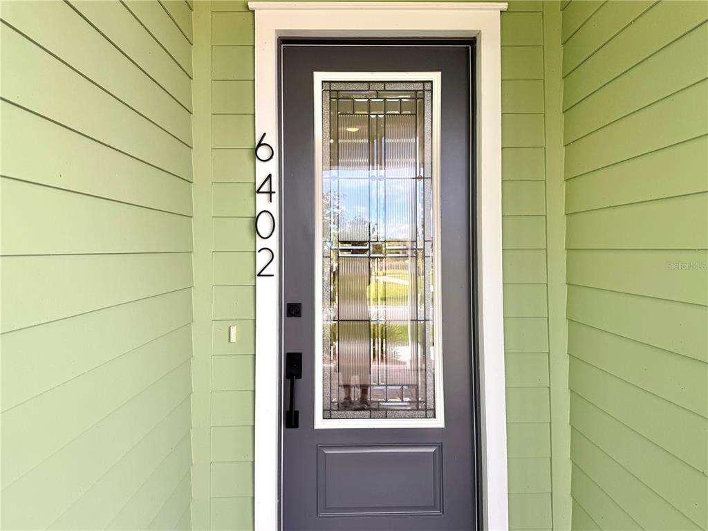 A front door with a glass insert and vertical house numbers on light green siding — 6402 ROVER WAY, ST CLOUD, FL