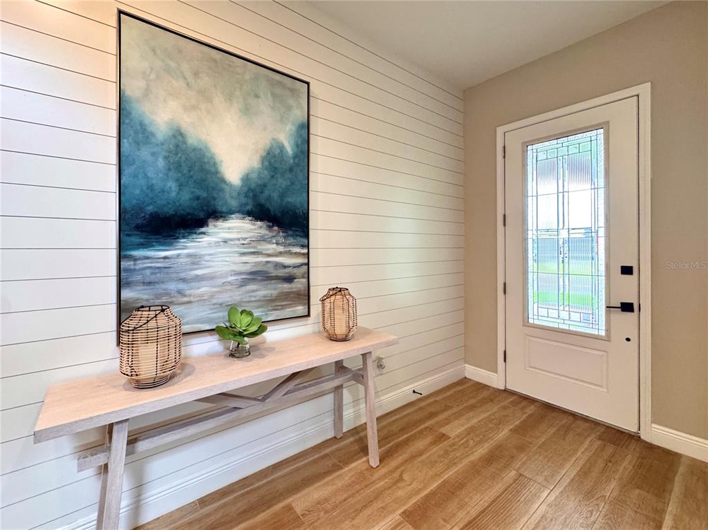 An entryway features a shiplap wall, a console table, artwork, and a glass-paneled front door — 6402 ROVER WAY, ST CLOUD, FL