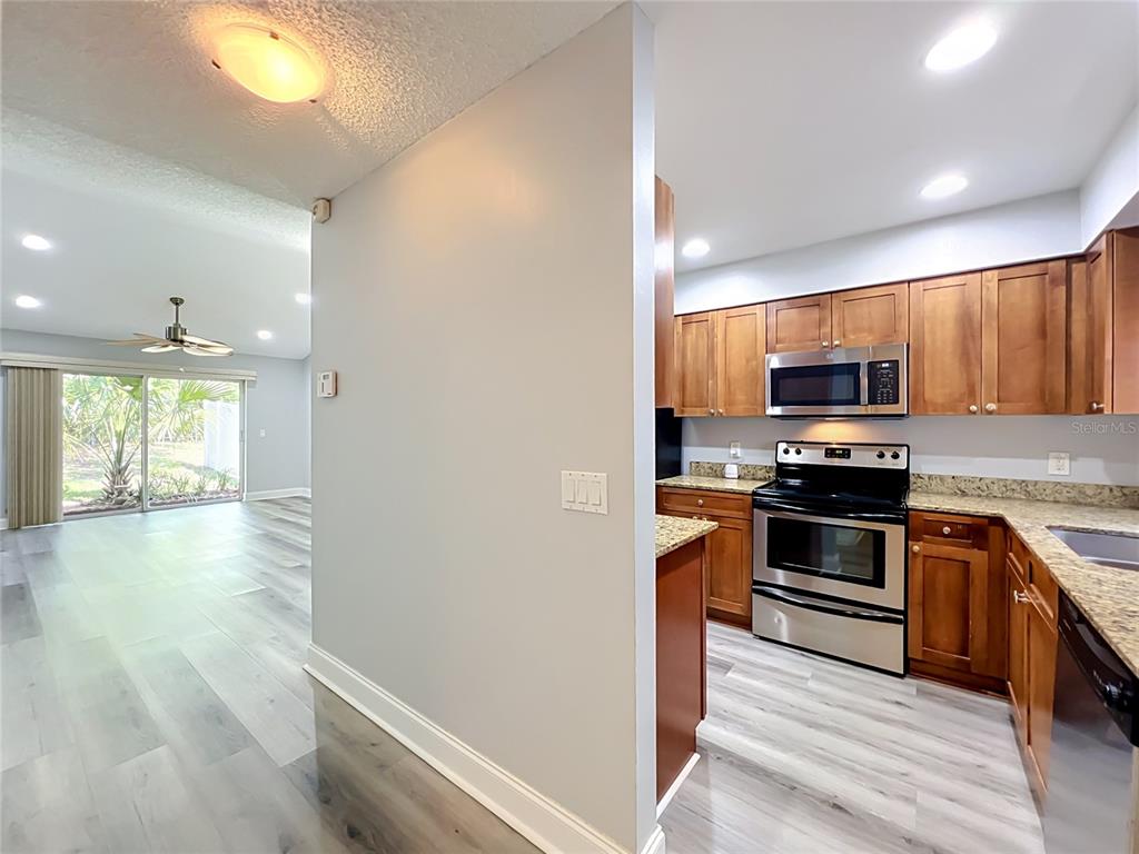 A kitchen with wood cabinets and stainless steel appliances opens to a living area — 5440 E MICHIGAN STREET UNIT 5440-2, ORLANDO, FL