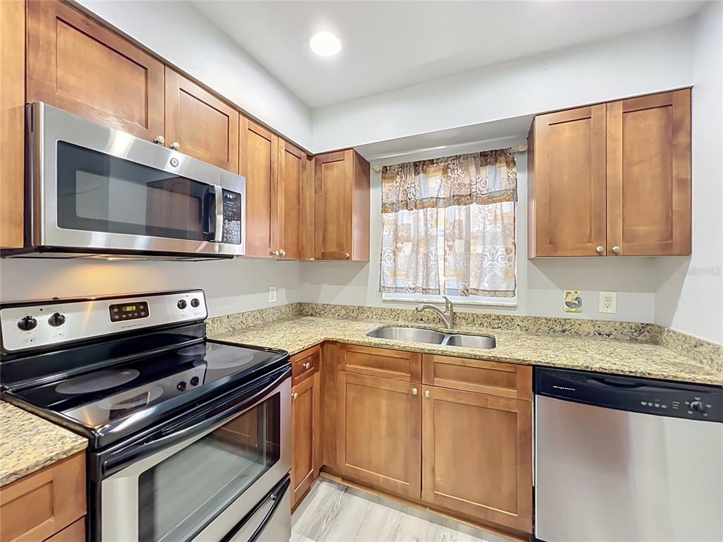 A kitchen features wood cabinets, granite countertops, stainless steel appliances, and a double sink — 5440 E MICHIGAN STREET UNIT 5440-2, ORLANDO, FL