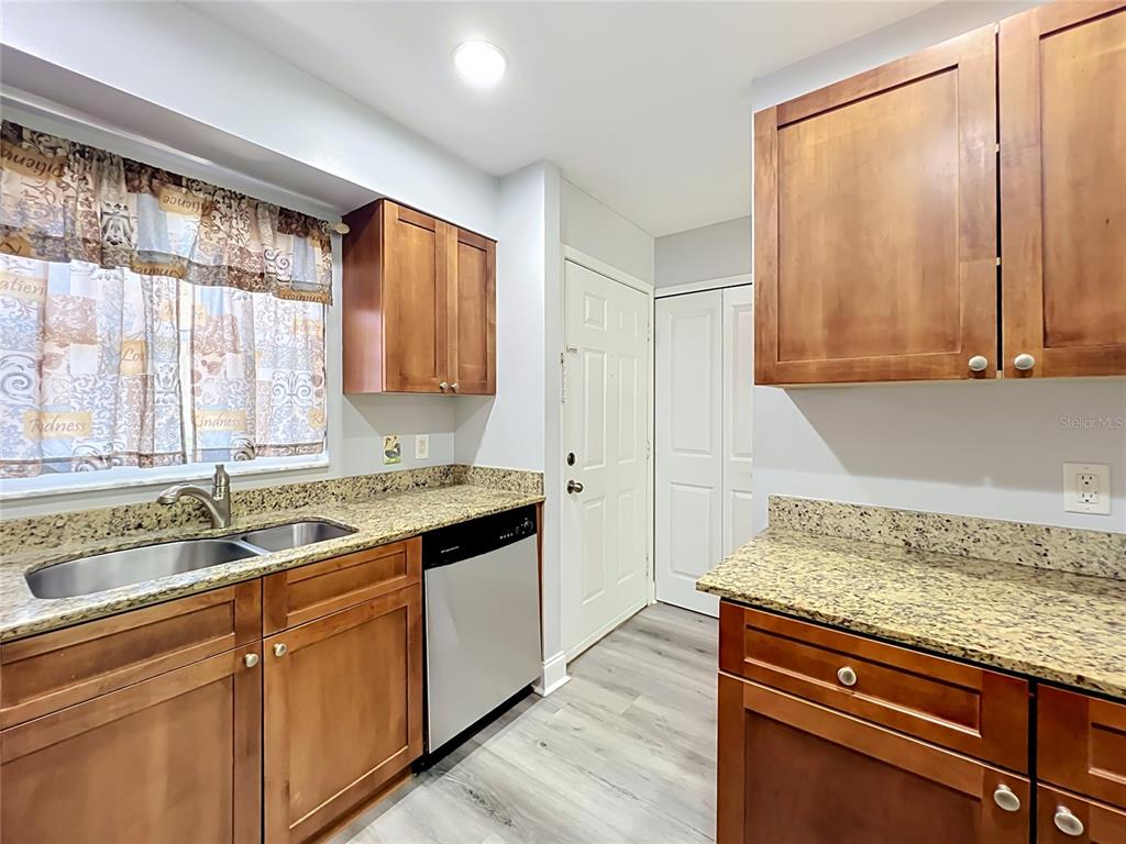 A kitchen features wood cabinets, granite countertops, a stainless steel dishwasher, and light-colored flooring — 5440 E MICHIGAN STREET UNIT 5440-2, ORLANDO, FL