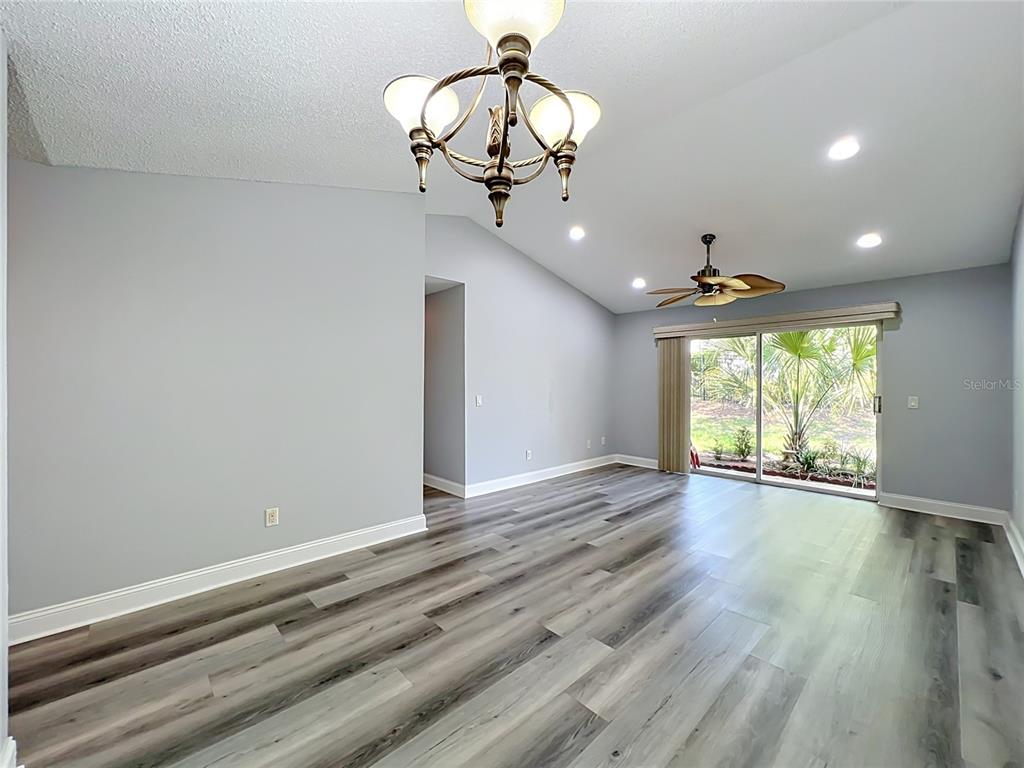 A living room features gray walls, wood-look flooring, a chandelier, a ceiling fan, and sliding doors — 5440 E MICHIGAN STREET UNIT 5440-2, ORLANDO, FL
