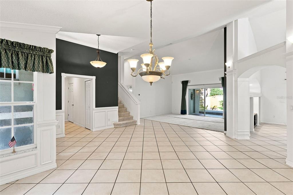 A spacious living area features tiled floors, a chandelier, a staircase, and a sliding glass door — 1490 BENT OAKS BOULEVARD, DELAND, FL