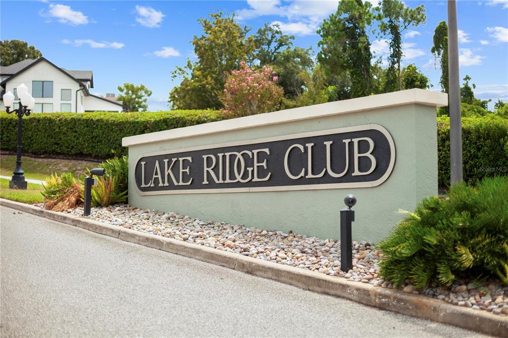 A light green monument sign reads Lake Ridge Club in front of a landscaped hedge — 12615 CROWN POINT CIRCLE, CLERMONT, FL