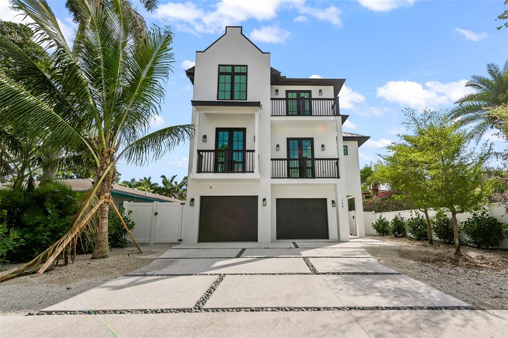 A three-story white house with two garage doors and balconies under a blue sky — 128 FILLMORE DRIVE, SARASOTA, FL