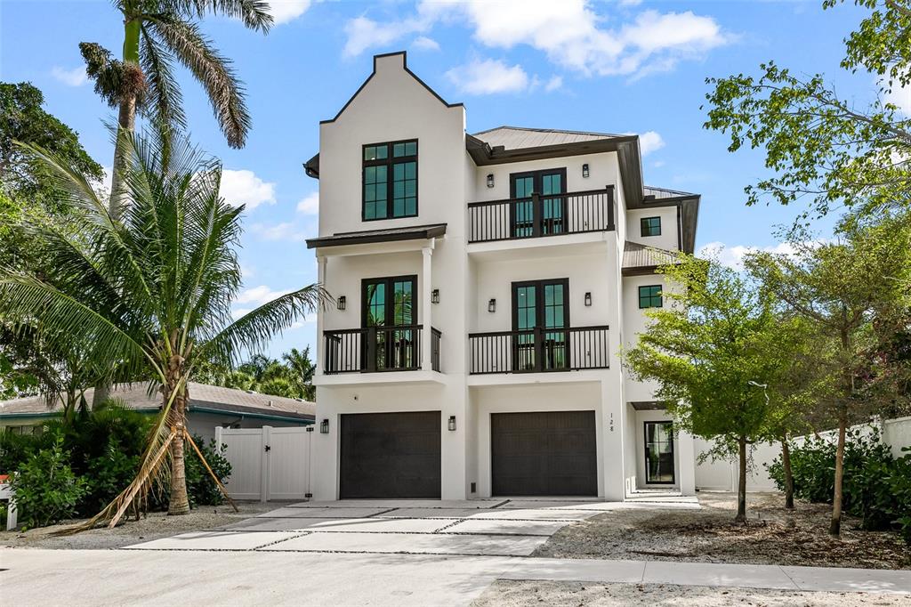 A three-story white house with two garages, balconies, and a palm tree in front — 128 FILLMORE DRIVE, SARASOTA, FL