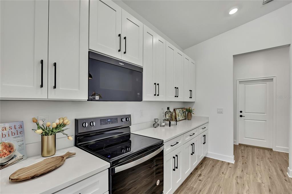A kitchen features white cabinets, a black microwave, a black electric stove, and white countertops — 13126 MEADOW SWALLOW AVENUE, BROOKSVILLE, FL