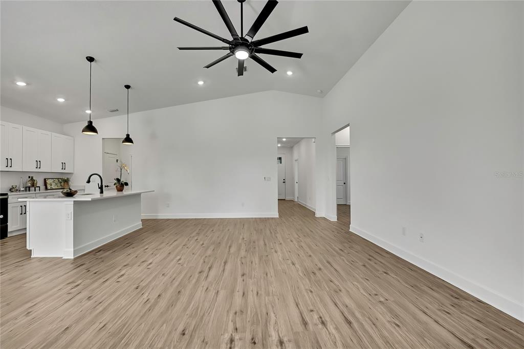 An open-concept kitchen and living area features white cabinetry, a large island, and wood-look flooring — 13126 MEADOW SWALLOW AVENUE, BROOKSVILLE, FL