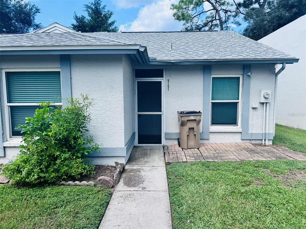 A single-story house exterior features a light-colored facade, a front door with a screen, and windows — 5151 GAINSVILLE DRIVE, TEMPLE TERRACE, FL