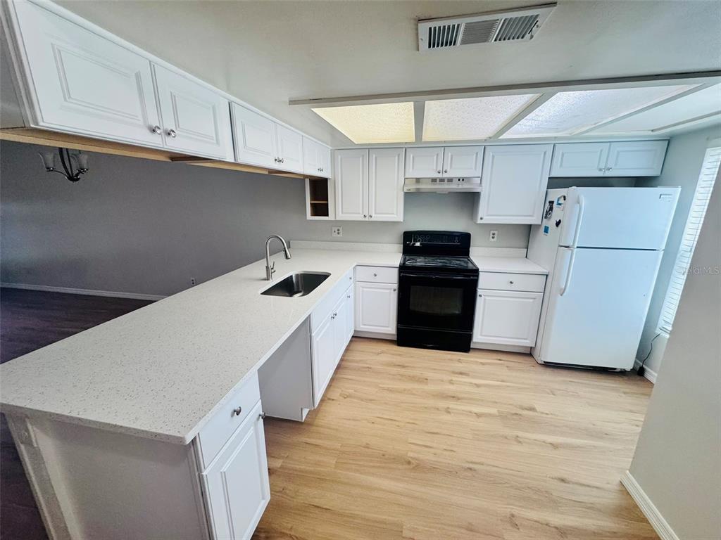 A kitchen features white cabinets, light countertops, a black stove, and light wood-look flooring — 5151 GAINSVILLE DRIVE, TEMPLE TERRACE, FL