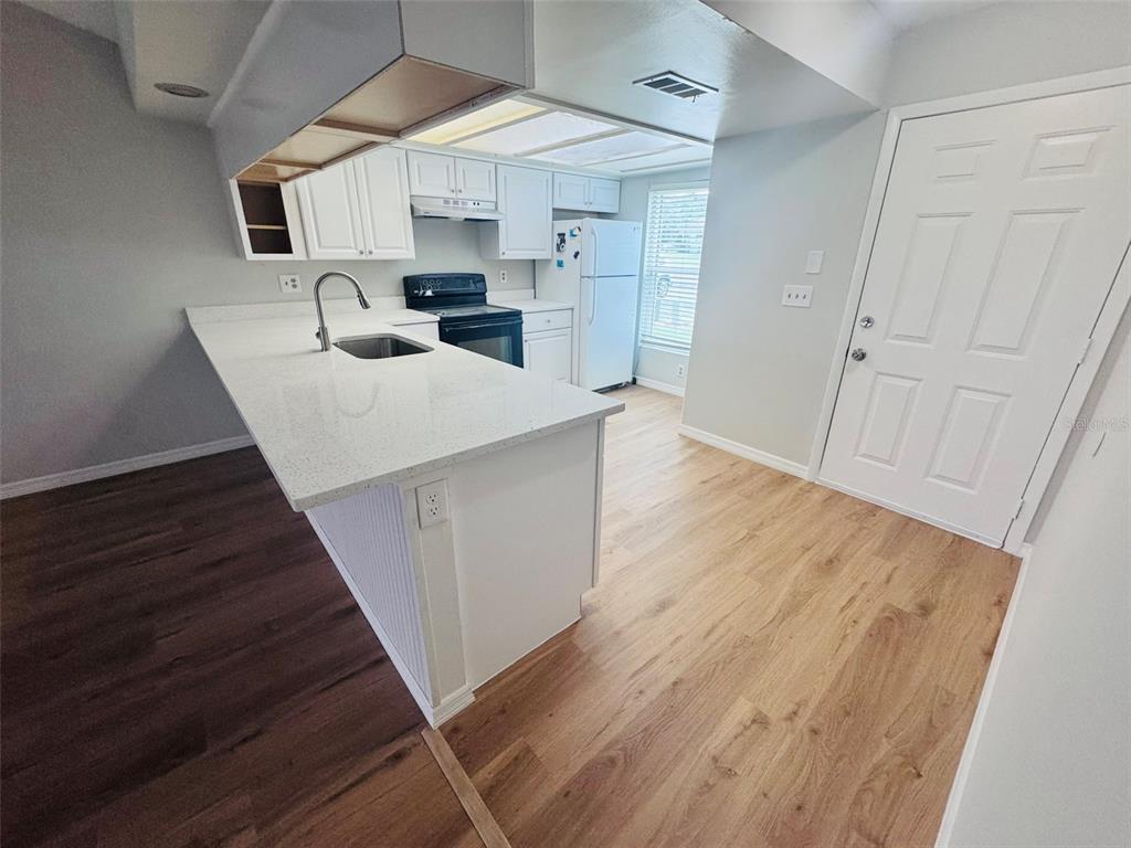 A kitchen features white cabinets, a quartz countertop island, and light wood-look flooring — 5151 GAINSVILLE DRIVE, TEMPLE TERRACE, FL