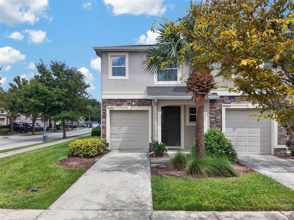 A two-story townhouse with a stone facade, two garage doors, and a palm tree out front — 10406 ORCHID MIST COURT, RIVERVIEW, FL