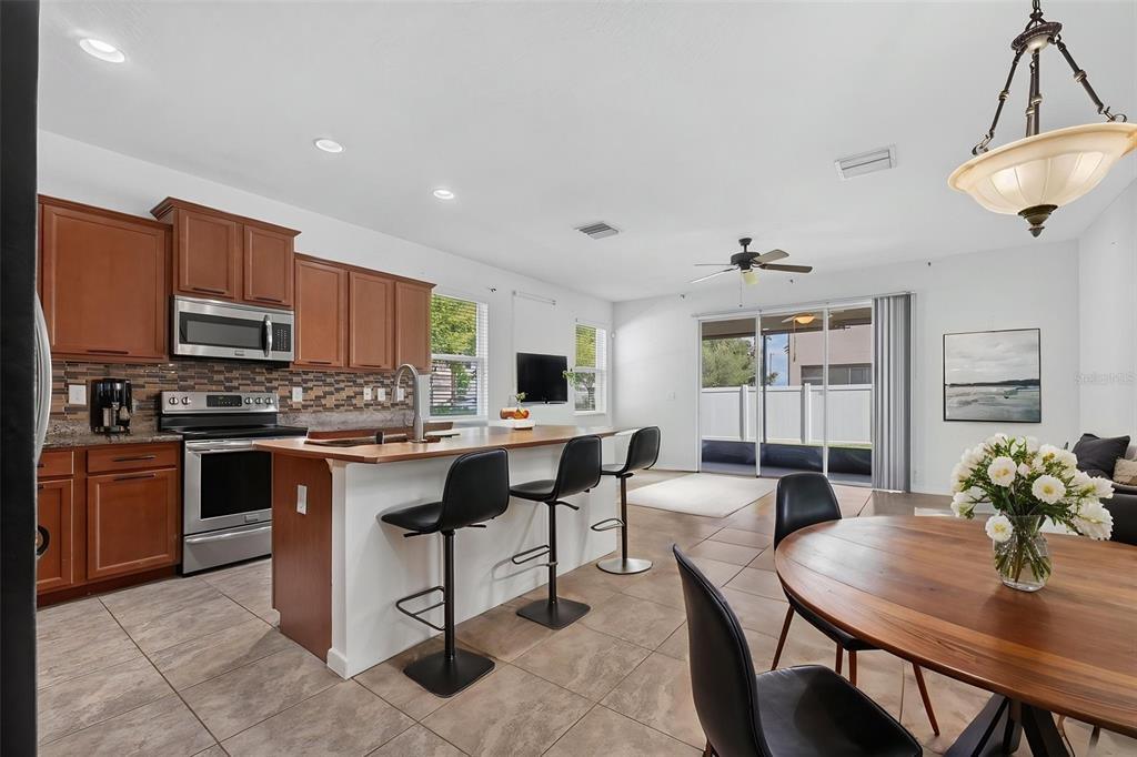 A kitchen with wood cabinets and a breakfast bar opens to a dining area — 10406 ORCHID MIST COURT, RIVERVIEW, FL