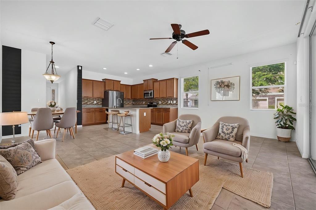 An open-concept living area features a kitchen with wood cabinets, tile floors, and furniture — 10406 ORCHID MIST COURT, RIVERVIEW, FL