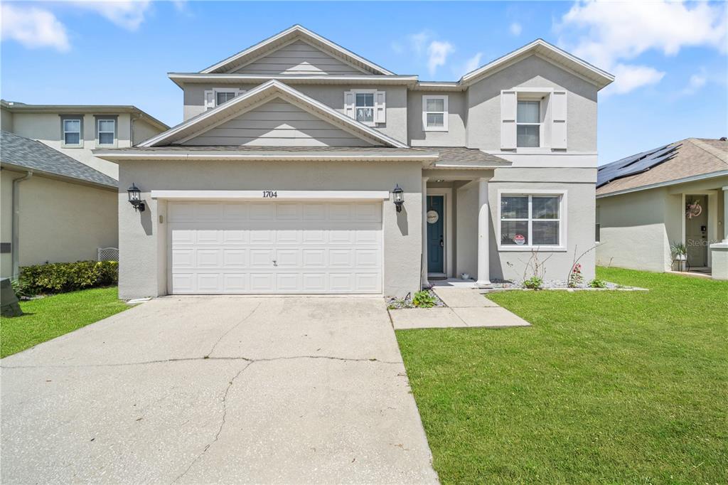 A two-story suburban house with a beige stucco exterior, a two-car garage, and a lawn — 1704 PINE RIDGE DRIVE, DAVENPORT, FL