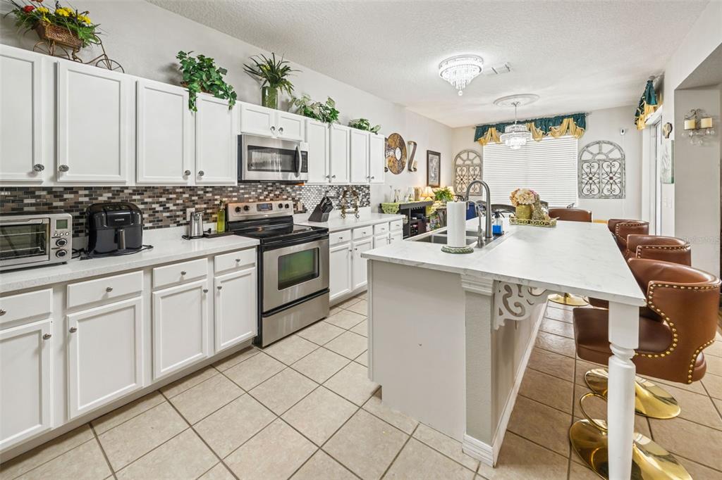 A kitchen features white cabinets, stainless steel appliances, a marble-topped island, and brown bar stools — 1704 PINE RIDGE DRIVE, DAVENPORT, FL
