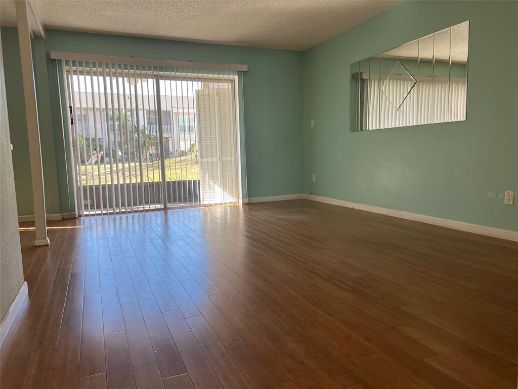 An empty living room features light green walls, wood-look flooring, and a large sliding glass door — 2625 STATE ROAD 590 UNIT 2514, CLEARWATER, FL