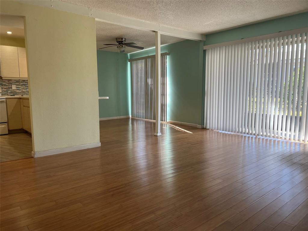 An open-concept living area features light wood flooring, pale green walls, and vertical window blinds — 2625 STATE ROAD 590 UNIT 2514, CLEARWATER, FL