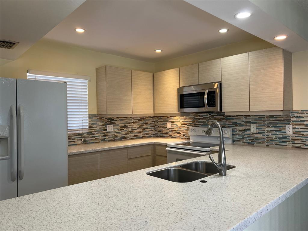 A kitchen features light wood cabinets, speckled countertops, a mosaic tile backsplash, and stainless appliances — 2625 STATE ROAD 590 UNIT 2514, CLEARWATER, FL
